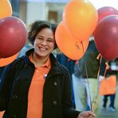 Young woman, wearing an orange shirt, standing beside orange and maroon balloons